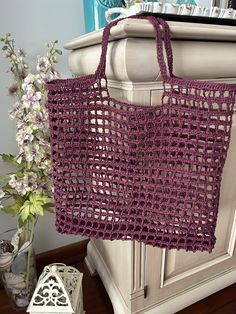 a purple crocheted bag sitting on top of a table next to a vase with flowers