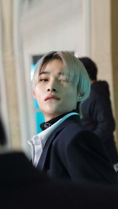 a young man with short hair wearing a black suit and white collared shirt, looking off into the distance