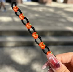 a hand holding an orange and black string with beads on it's end, in front of a sidewalk