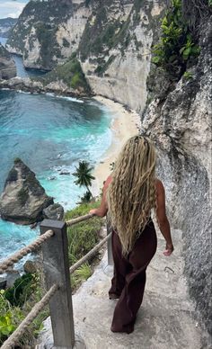 a woman with long blonde hair walking up stairs to the beach