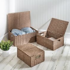 three wicker storage baskets on the floor next to a potted plant and blanket