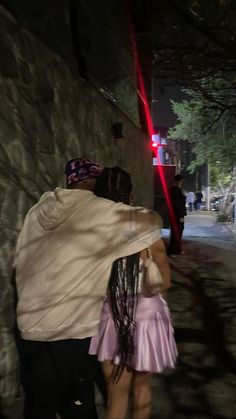 a woman in a pink dress walking down a street next to a man wearing a white jacket