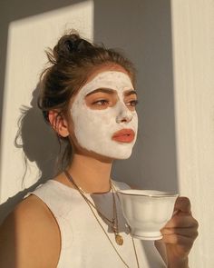 a woman with white facial mask holding a cup