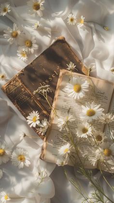 an open book laying on top of a bed covered in daisies