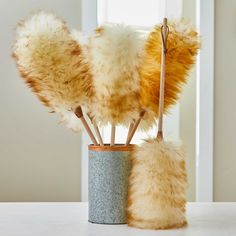 two vases filled with fake fur on top of a white table next to a window