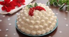 a cake with white frosting and berries on top sitting on a table next to red poinsettis