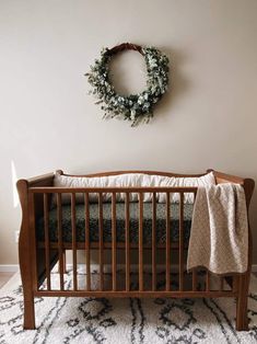 a baby crib with a wreath on the wall above it and a rug underneath