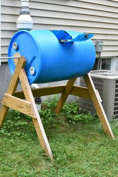 a large blue barrel sitting on top of a wooden stand in the grass next to a house