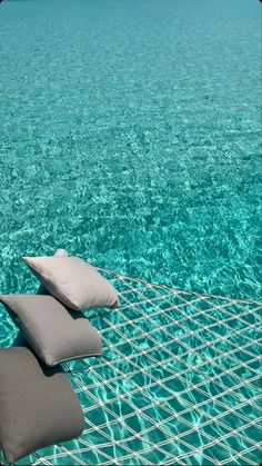 three pillows sitting on top of a metal net in the middle of clear blue water