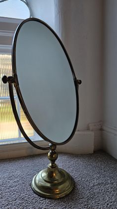 a round mirror sitting on top of a metal stand in front of a windowsill