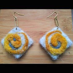 the earrings are made out of yarn and have yellow, white and blue designs on them