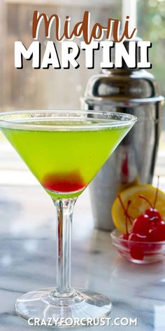 a green martini sitting on top of a table next to a potted lemon and cherries