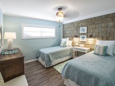 two beds in a room with wood flooring and brick wall on the walls behind them