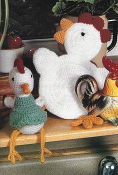 two knitted chickens and a chicken on top of a wooden shelf next to a potted plant