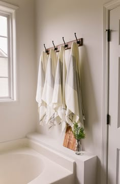 towels hanging on the hooks above a bathtub with a cutting board next to it