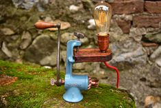 a small blue machine with a light bulb on it's head sitting on a mossy surface