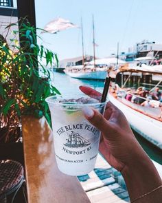 a person holding up a drink in front of the water