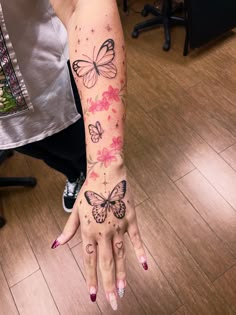 a woman's hand with butterflies on it and pink flowers in the middle of her arm