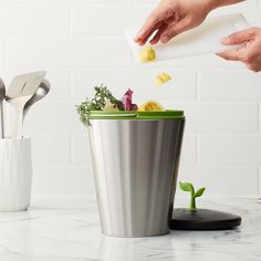 a person is throwing food into a trash can with utensils in the background