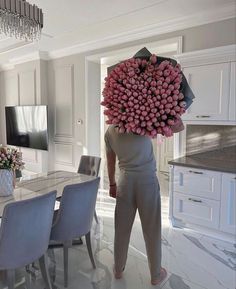 a person with a bunch of flowers on their head standing in front of a dining room table