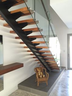 a chair sitting under a stair case next to a wooden handrail and glass railing