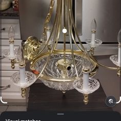 a gold chandelier with candles on it in front of a silver refrigerator freezer