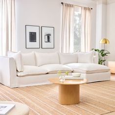 a living room filled with white furniture and curtains on the window sill, next to a coffee table