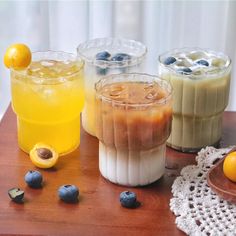 three glasses filled with different types of drinks on top of a wooden table next to oranges and blueberries