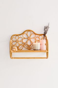 two candles sitting on top of a bamboo shelf next to some flowers and plants in front of a white wall