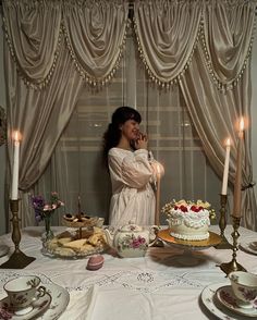 a woman standing in front of a table with cake and tea cups on top of it