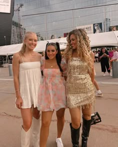 three young women standing next to each other in front of a building with people walking around