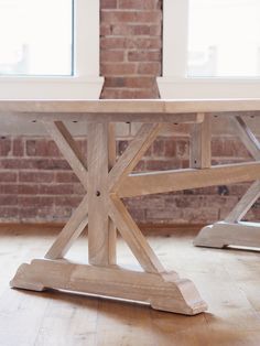 a wooden table sitting in front of a window next to a brick wall and floor