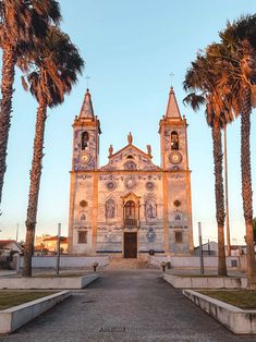 an old church surrounded by palm trees on a sunny day with the sun going down