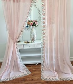 pink curtains with white trim and flowers in vase on table next to mirror at home