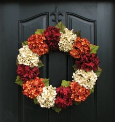 a wreath with red, white and orange flowers is hanging on a black front door