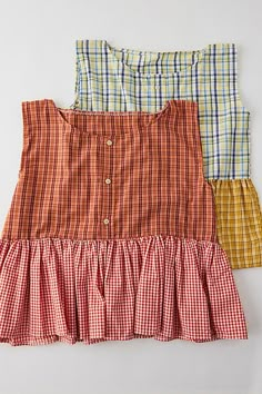 three different plaid dresses are lined up on a white surface, one is orange and the other is yellow