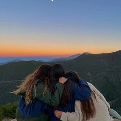 two women hugging each other on top of a mountain at sunset with the moon in the sky