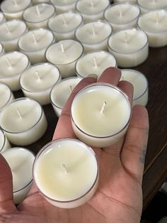 two hands holding small white candles in front of rows of smaller ones