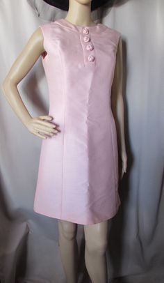 "Simply sophisticated spring or summer sheath in lovely shade of pink.  Designed by Maggi, It is princess seamed with banded jewel neckline. The front placket has 4 self-fabric coiled decorative buttons.  The dress is sleeveless and meant to be above the knee. It closes at the back with 20\" nylon zipper. It is lined. The fabric is similar to a linen in weave and weight. We could not trace the Maggi label, but would place this in the late 1980/1990 or early 2000's.    Size: label says size 11. B Princess Seams Dress, Pink Sleeveless Formal Dress For Summer, Elegant Pink Fitted Sleeveless Dress, Feminine Pink Sleeveless Dress For Formal Occasion, Spring Pink Sleeveless Dress For Formal Occasions, Spring Formal Pink Sleeveless Dress, Spring Pink Sleeveless Formal Dress, Pink Sleeveless Dress For Spring Formal, Fitted Pink Lined Sleeveless Dress