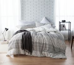 a bedroom with white brick walls and wooden flooring is pictured in this image, the bed has an overstuffed comforter on it's side