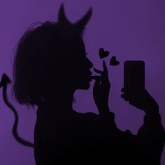 a woman holding a cell phone in front of her face with devil horns on it