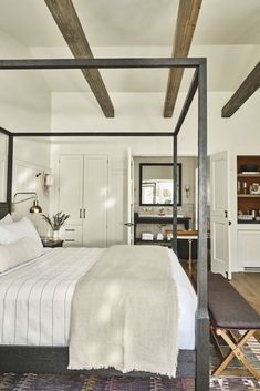 a bedroom with a four poster bed, white walls and wooden beams on the ceiling