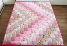 a pink and white quilt on top of a wooden bed in a room with hard wood flooring