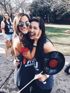 two young women are hugging each other while one holds a record and the other is holding a stick