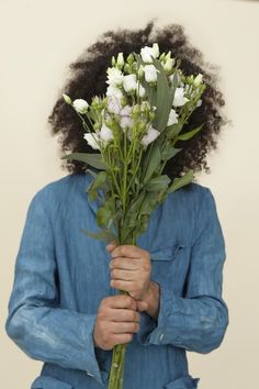 a woman holding flowers in her hands and looking at the camera while wearing a blue shirt