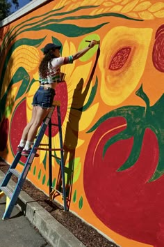 a woman is painting a mural on the side of a building in front of a ladder