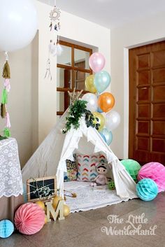 a teepee tent with balloons and decorations on the floor, next to a birthday cake