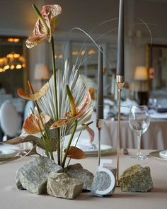 there is a vase with flowers and rocks on the table in front of some candles