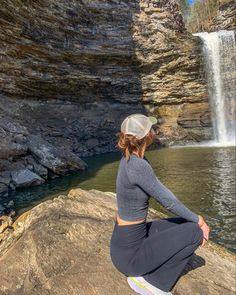 a woman sitting on top of a rock next to a waterfall