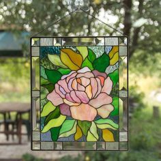 a stained glass window with a pink rose on it and green leaves hanging from the outside